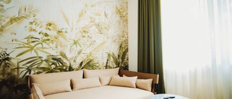 A room with a sofa, a round table, and a wall with a tropical plant mural.
