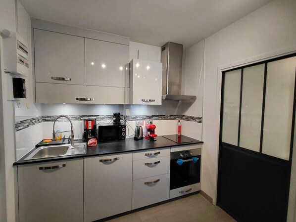 A compact kitchen with white cabinets, a stainless steel sink, a black countertop, and a built-in oven. - Grand Studio rénové, tout confort - Résidence du Bois de l'ours (Les Rousses)