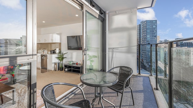 Een balkon met een glazen deur naar een keuken, een eettafel met stoelen en uitzicht op de stadsgezicht.