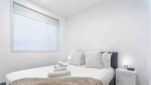 Een slaapkamer met een bed, kussens, een nachtkastje en een raam.
