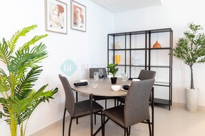 Un coin repas avec une table ronde, quatre chaises, une bibliothèque noire et deux plantes en pot.