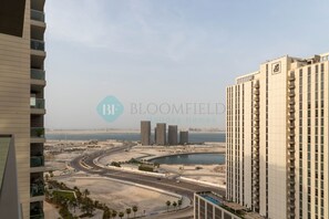 Un immeuble de grande hauteur doté de nombreux balcons, offrant une vue sur une route côtière et sur une étendue d’eau en arrière-plan.