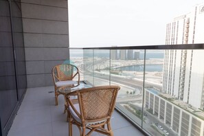 Ein Balkon mit Korbstühlen und einem Glastisch mit Blick auf eine Stadtlandschaft, einschließlich Wolkenkratzer und einer Brücke.