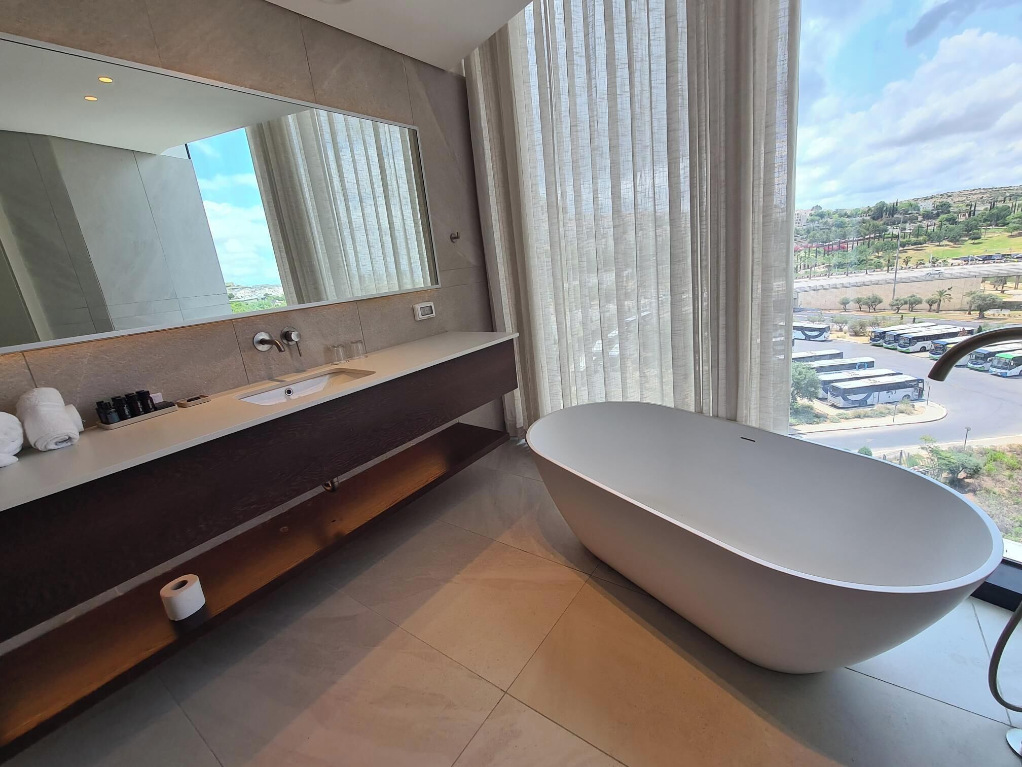 A modern bathroom with a large bathtub, a vanity with a mirror, and a view of a parking area.