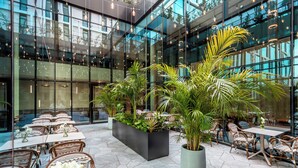 A modern indoor patio with glass walls, outdoor seating, and potted plants. - Jacob Modi'in (Modi'in-Maccabim-Re'ut)