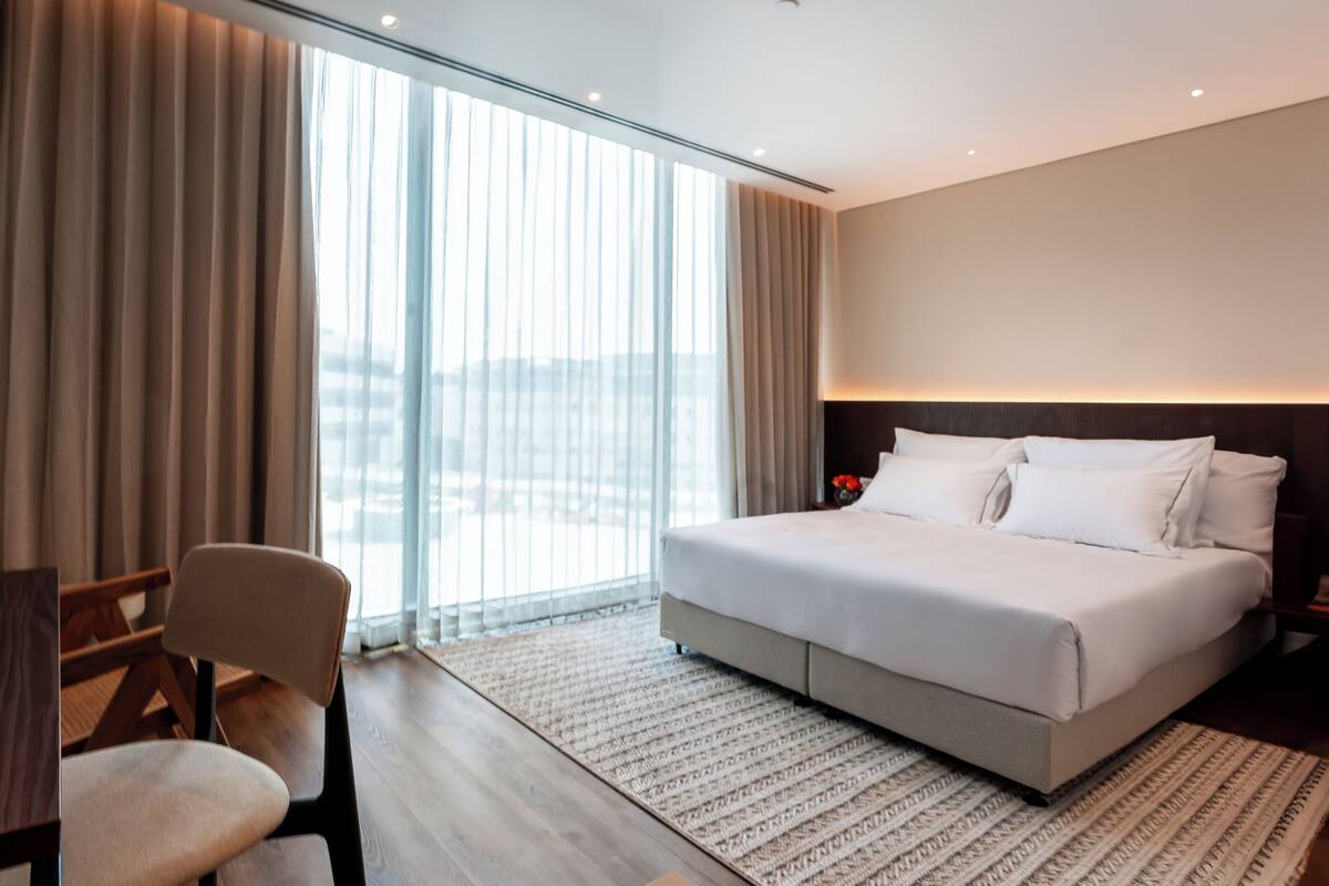 A modern hotel room with a large bed, a desk, and a chair.