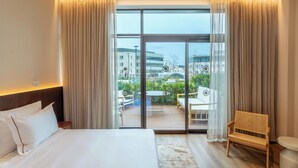 A hotel room with a large bed, a wooden chair, a small table, and a balcony with outdoor furniture. - Jacob Modi'in (Modi'in-Maccabim-Re'ut)