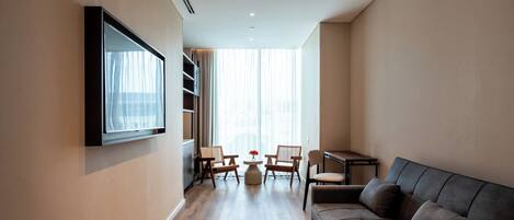 A modern living room with a sofa, two armchairs, a coffee table, and a TV mounted on the wall.