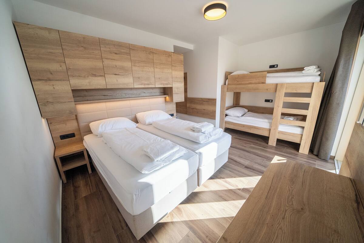 A modern bedroom with a bunk bed, two single beds, a wooden headboard, and a small table.
