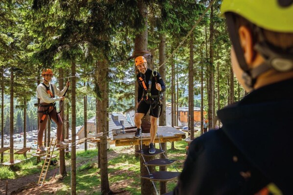 Dos personas en una plataforma suspendida en un área boscosa, usando arneses de seguridad y cascos.