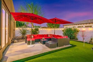 Eine Terrasse mit Gartenmöbeln, zwei roten Sonnenschirmen und einem gepflegten Rasen.