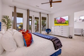 A bedroom with a bed, a dresser, a chair, and a window with a view of trees and a pink flower.