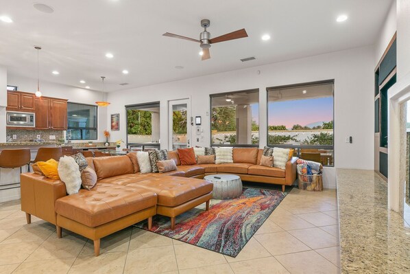 A spacious living area with a large sectional sofa, a round coffee table, and a ceiling fan.