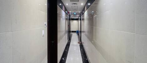 A modern hallway with white and black marble floors, recessed lighting, and a glass door on the left.