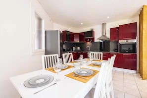Une cuisine moderne avec des meubles rouges, une table Ă manger blanche mise avec des assiettes et des verres, et une grande fenĂȘtre.