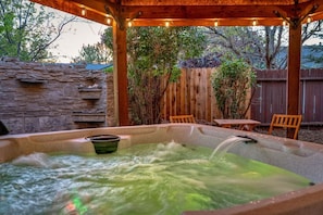 A hot tub with a stone wall and wooden fence in the background.