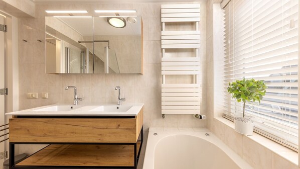 Une salle de bain moderne avec un meuble-lavabo en bois, une baignoire et un grand miroir.