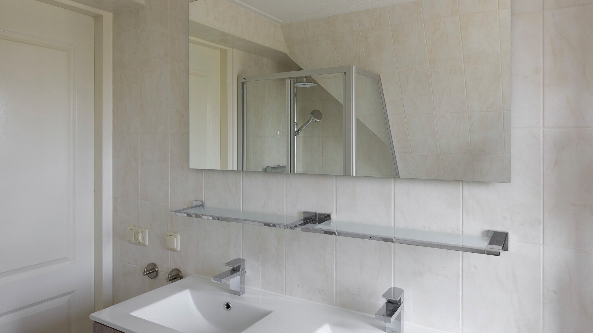 A modern bathroom with a white sink, a mirror above the sink, and a shower enclosure.