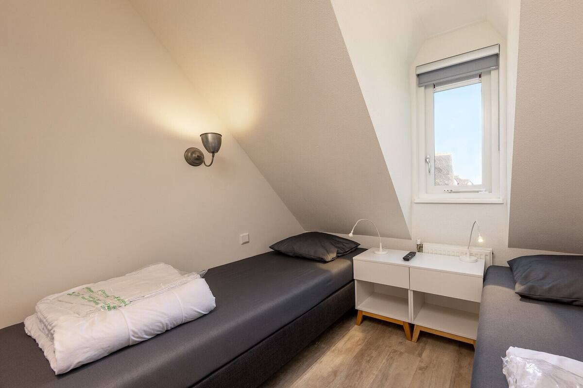 A small, modern bedroom with two beds, a desk, and a window.