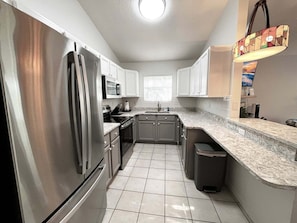 A modern kitchen with stainless steel appliances, white cabinetry, and a tiled floor.