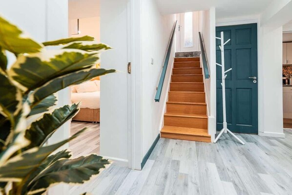 Una escalera que conduce a una puerta azul oscuro, una pared blanca y una planta al frente.