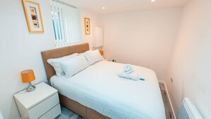 Een keurig opgemaakt slaapkamer met een bed, nachtkastjes en een raam met jaloezieën.