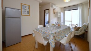 A dining area with a table set for four, a refrigerator, and a window with curtains. - A cozy haven for rest and recharging (San Michele Al Tagliamento)