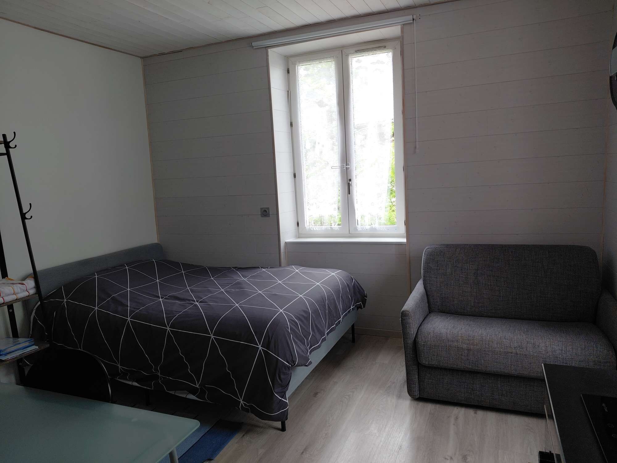 A bedroom with a bed, a chair, a window, and a coat rack.