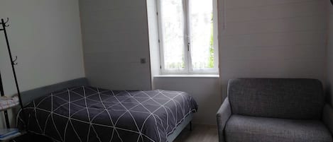 A bedroom with a bed, a chair, a window, and a coat rack.