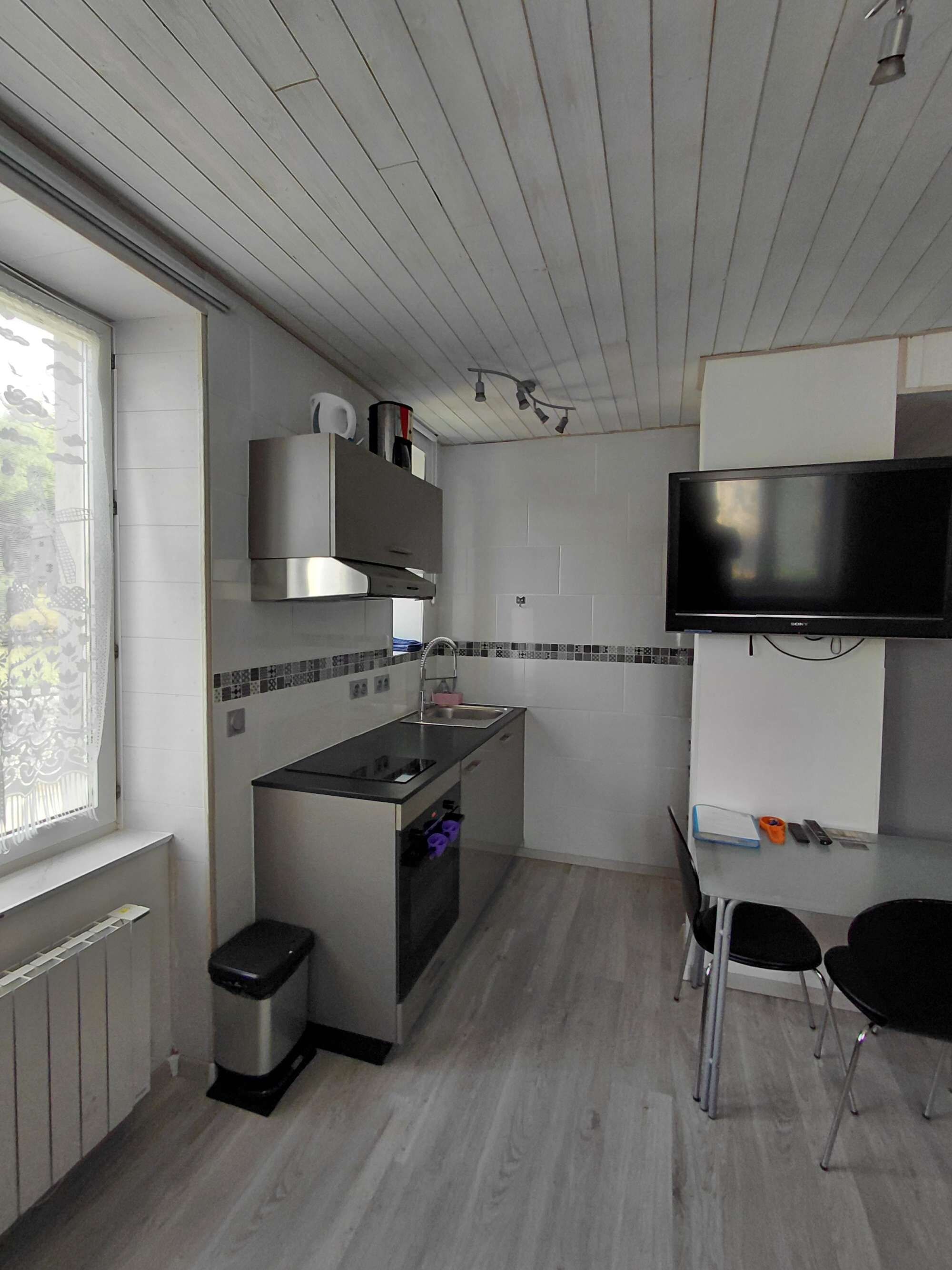 Een compacte keuken met een ingebouwde oven, een spoelbak en een kleine eethoek met twee stoelen.