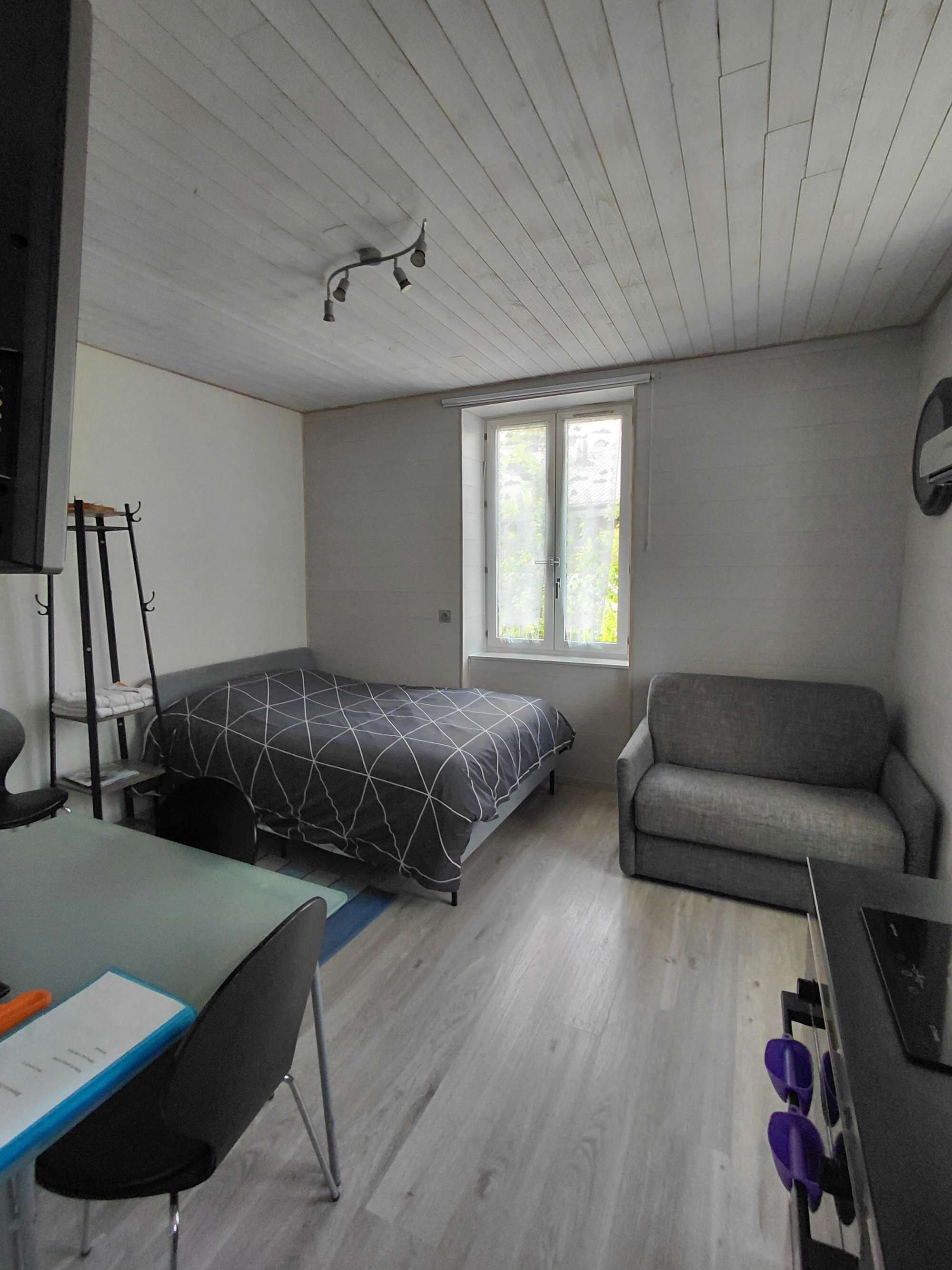 A room with a bed, a sofa, a desk with a chair, and a window.