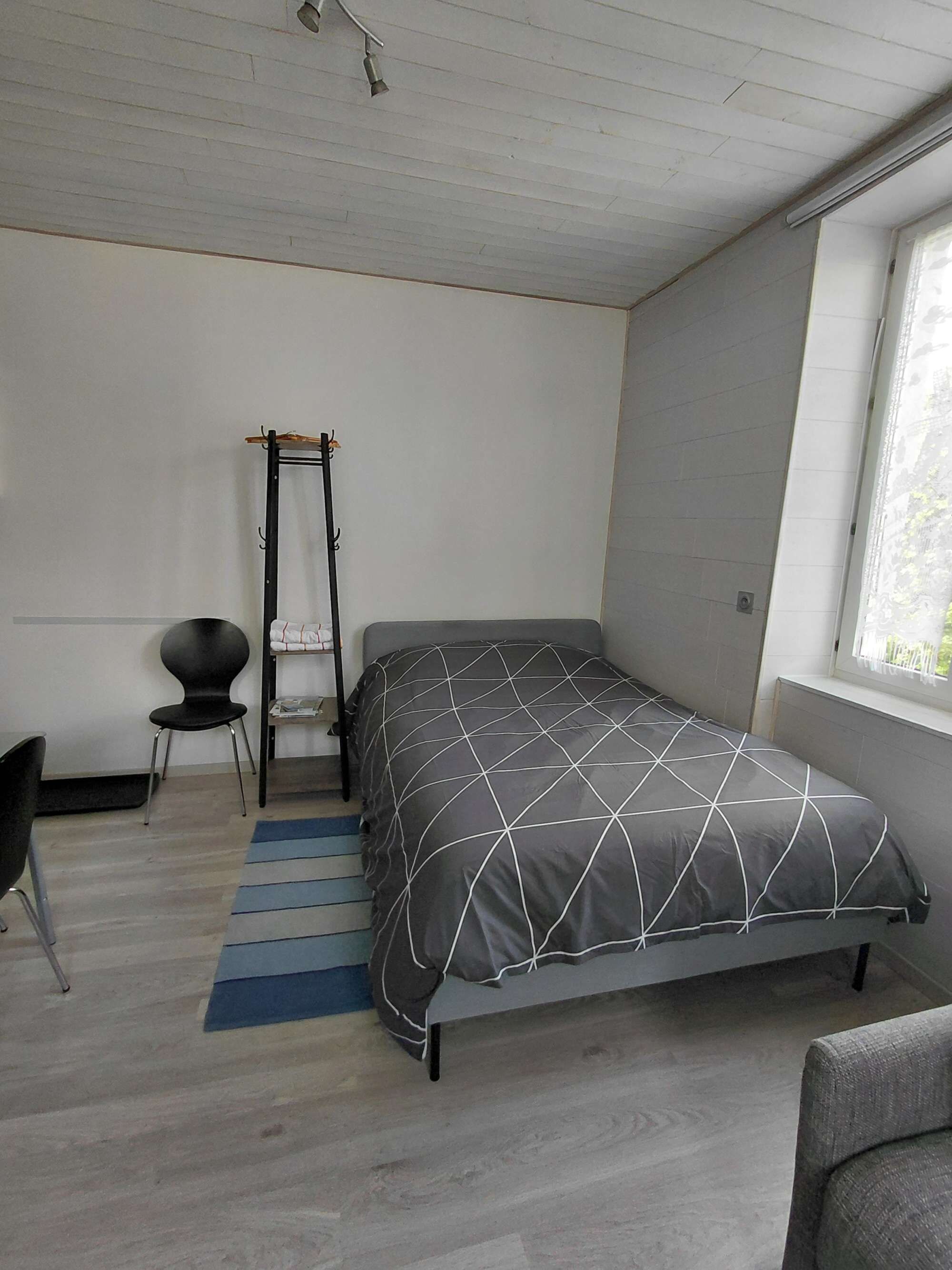 Une chambre à coucher avec un lit, une chaise, un porte-manteau et une fenêtre.