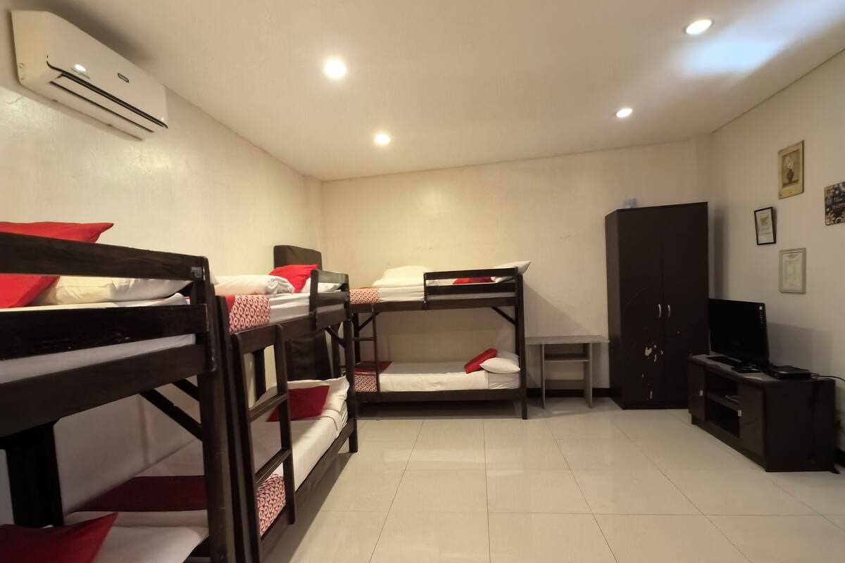 Une chambre de dortoir avec des lits superposés, une petite table, un téléviseur et une armoire.