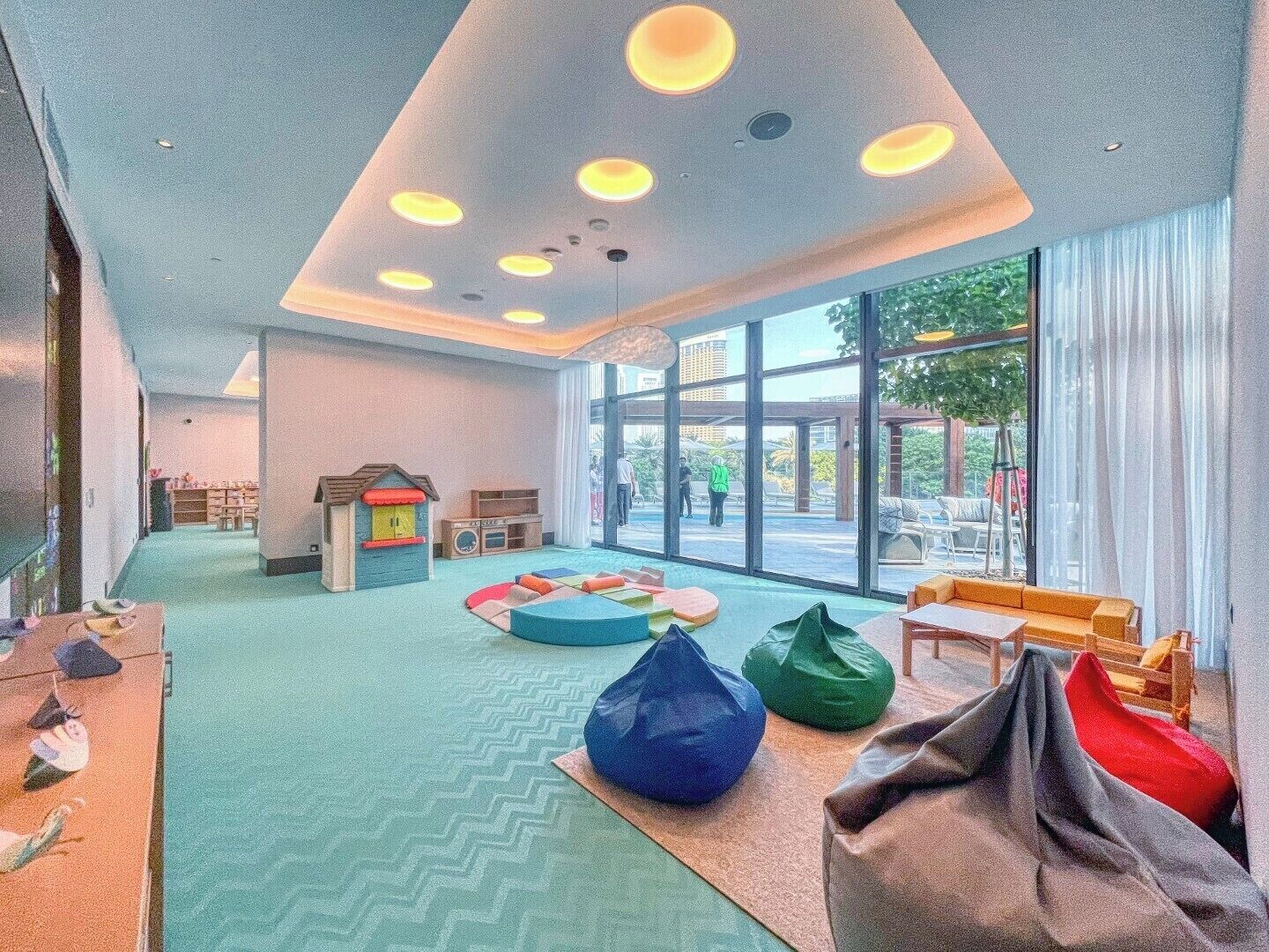 A spacious room with a large window, a play area with colorful bean bags, and a small playhouse.