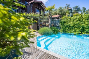A wooden deck surrounding a swimming pool with a wooden fence and lush greenery.