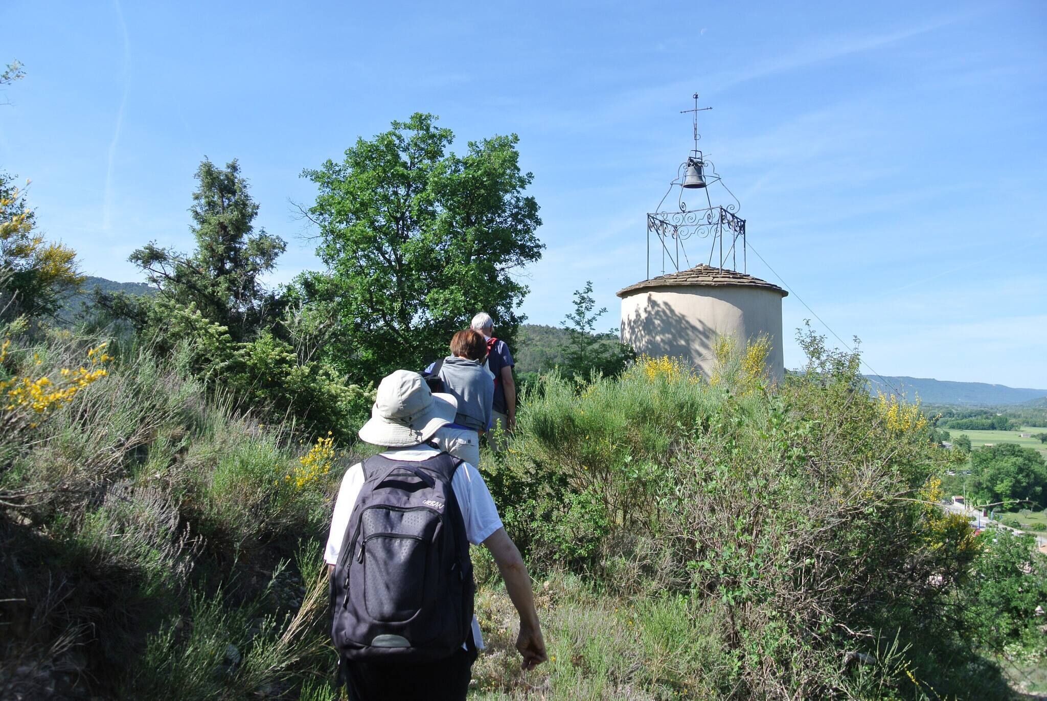 A person walking towards a cylindrical structure with a metal antenna on top, surrounded by greenery and trees.