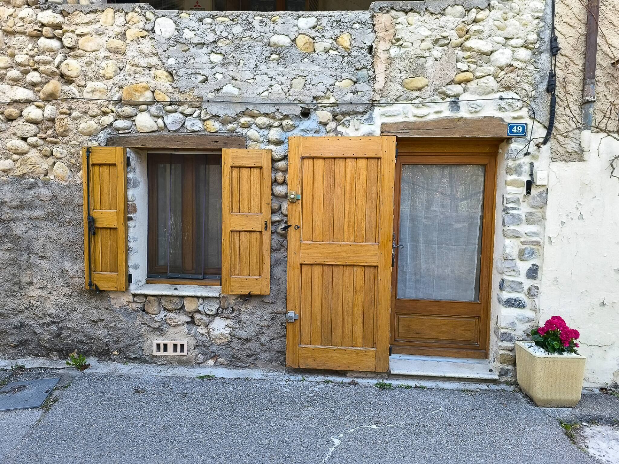 A stone building with two wooden doors and windows, a small vent, and a potted plant.