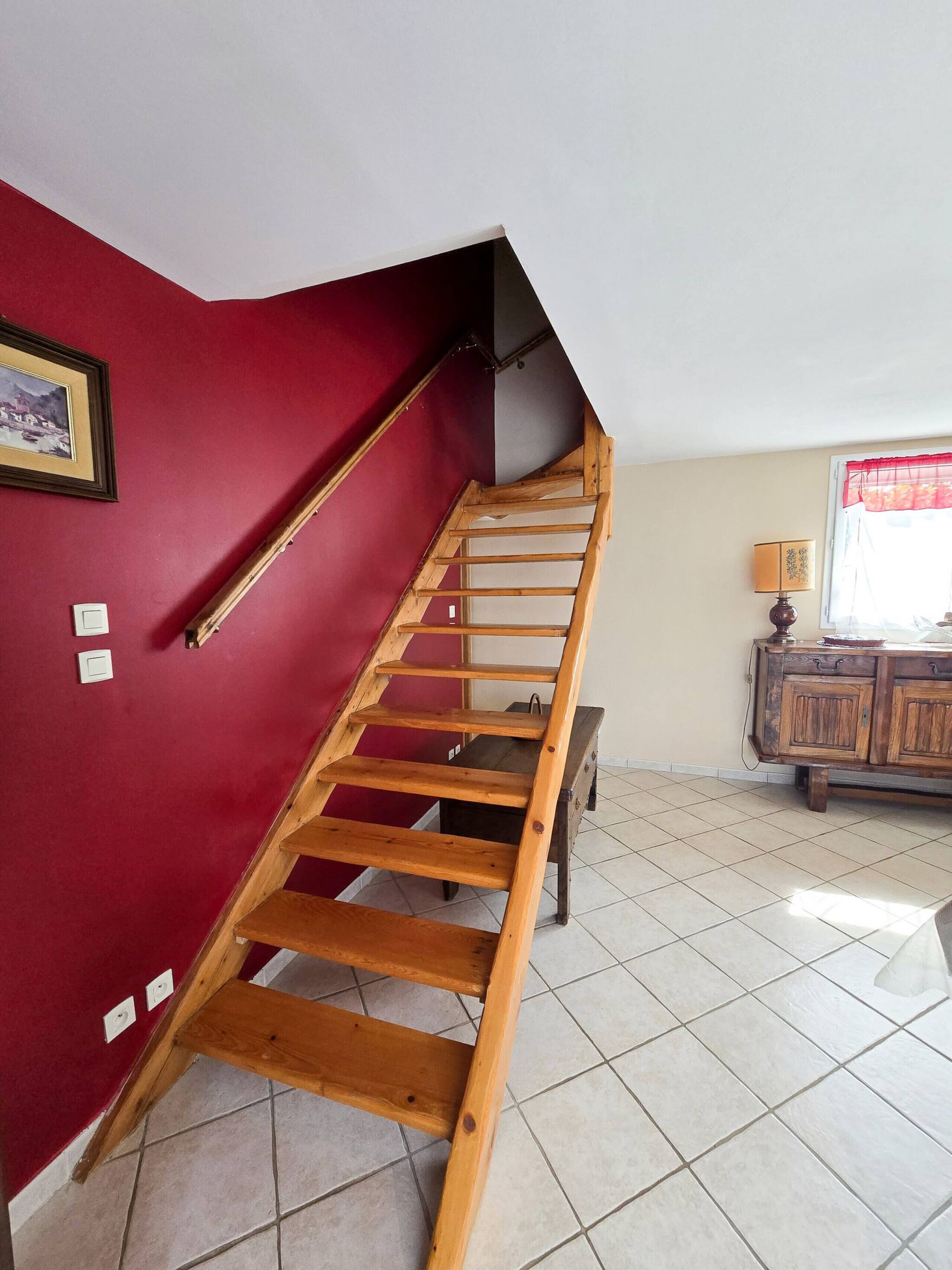 Un escalier en bois, avec un mur rouge et un sol carrelé.