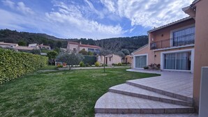 A residential area with a well-maintained lawn, a curved driveway leading to a house with a balcony, and a hilly backdrop. - Villa Bastide Volonne (Volonne)