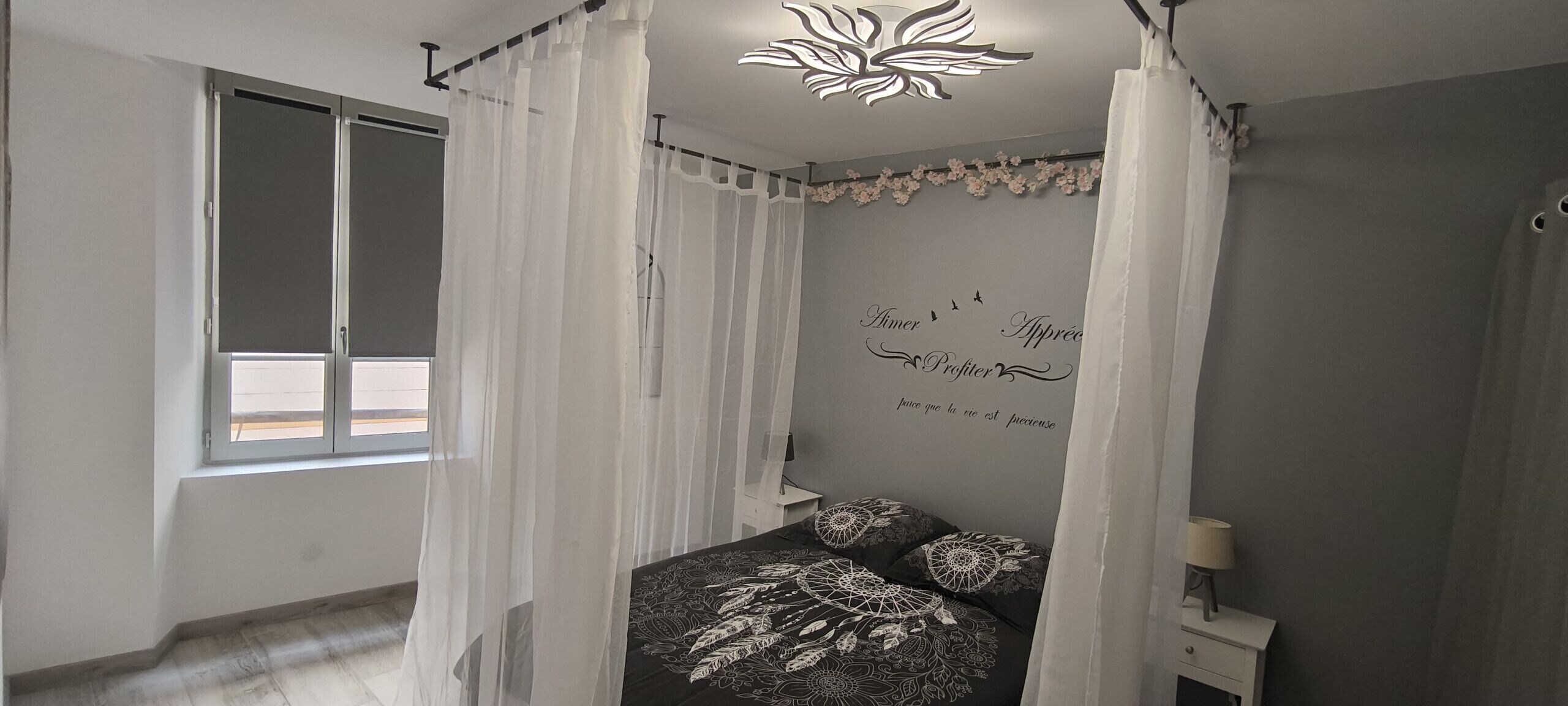 Camera da letto con un letto, una finestra, un comodino e una parete con testo decorativo.