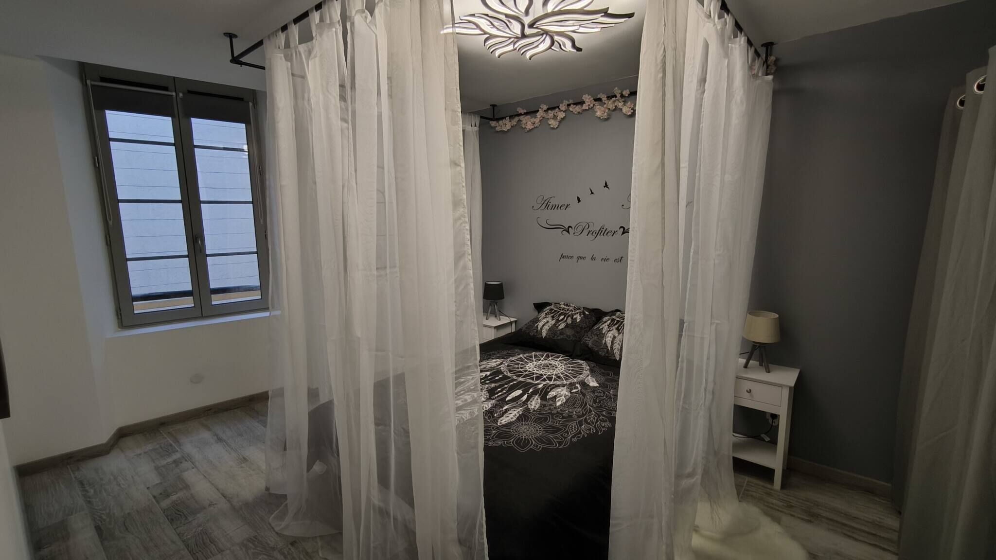 Un dormitorio con cama, mesita de noche, lámpara y ventana con cortinas.