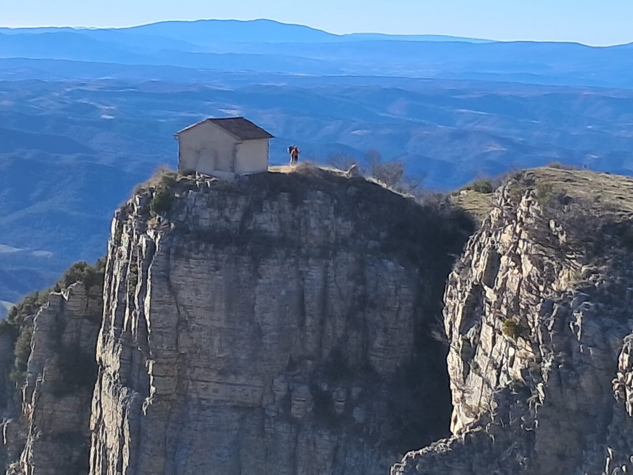 A small building on a cliff edge with a vast landscape in the background.