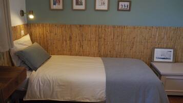 A bedroom with a bed, a bedside table, a wall-mounted lamp, and framed pictures.