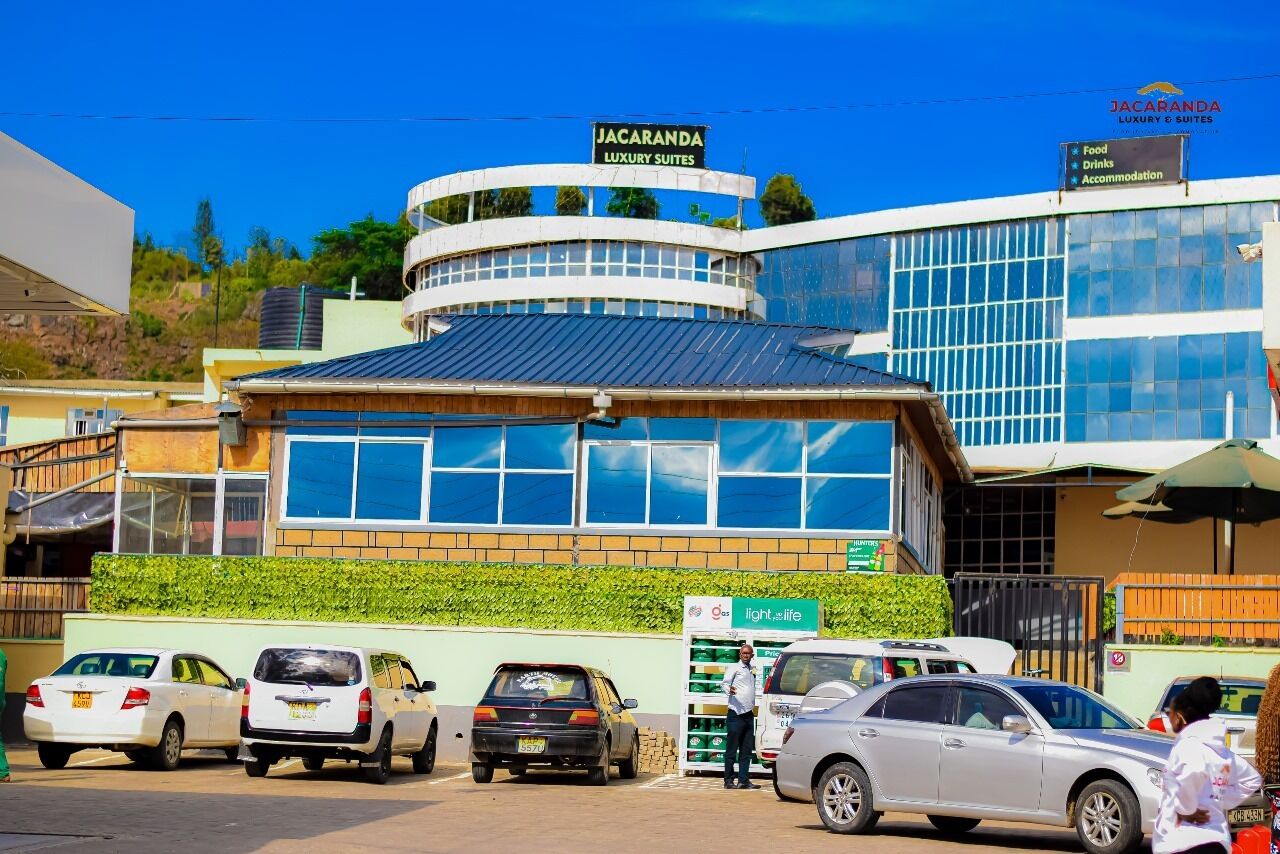 A building with a sign reading "JACARANDA LUXURY SUITES" and a sign for "Food, Drinks, Accommodation" nearby.