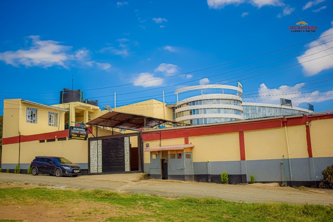A hotel with a yellow facade, a covered entrance, and a sign indicating it is a Jacaranda Luxury Suites.