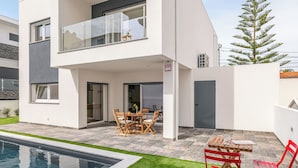 A modern two-story house with a swimming pool, outdoor seating, and a visible alarm sign. - Summer house with pool & garden, 5m ride to Caparica beach (Charneca da Caparica almada)