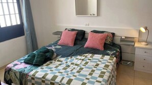 A single bed with a checkered bedspread, two pillows, a bedside lamp, and a mirror on the wall.