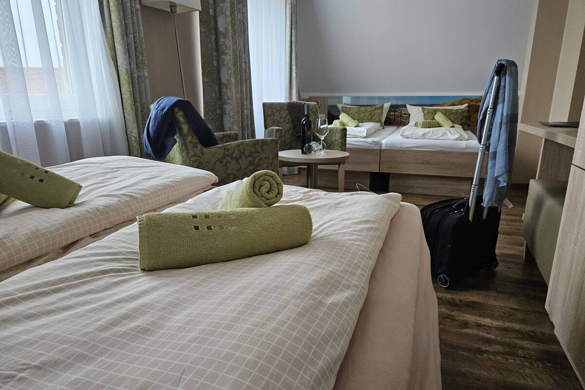 A hotel room with two beds, a chair, a table, and a suitcase.