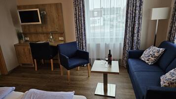 Hotelkamer met een bed, een bank, een bureau met stoel, een televisie bevestigd aan een houten paneel en een raam met gordijnen.
