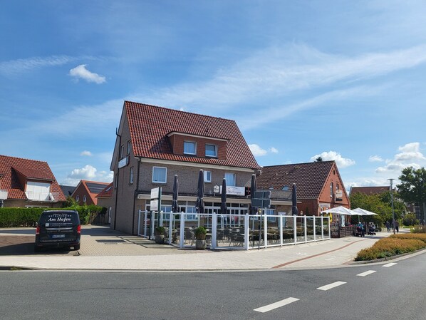 Un hôtel avec un toit recouvert de tuiles rouges, une entrée en verre et des places assises à l’extérieur.
